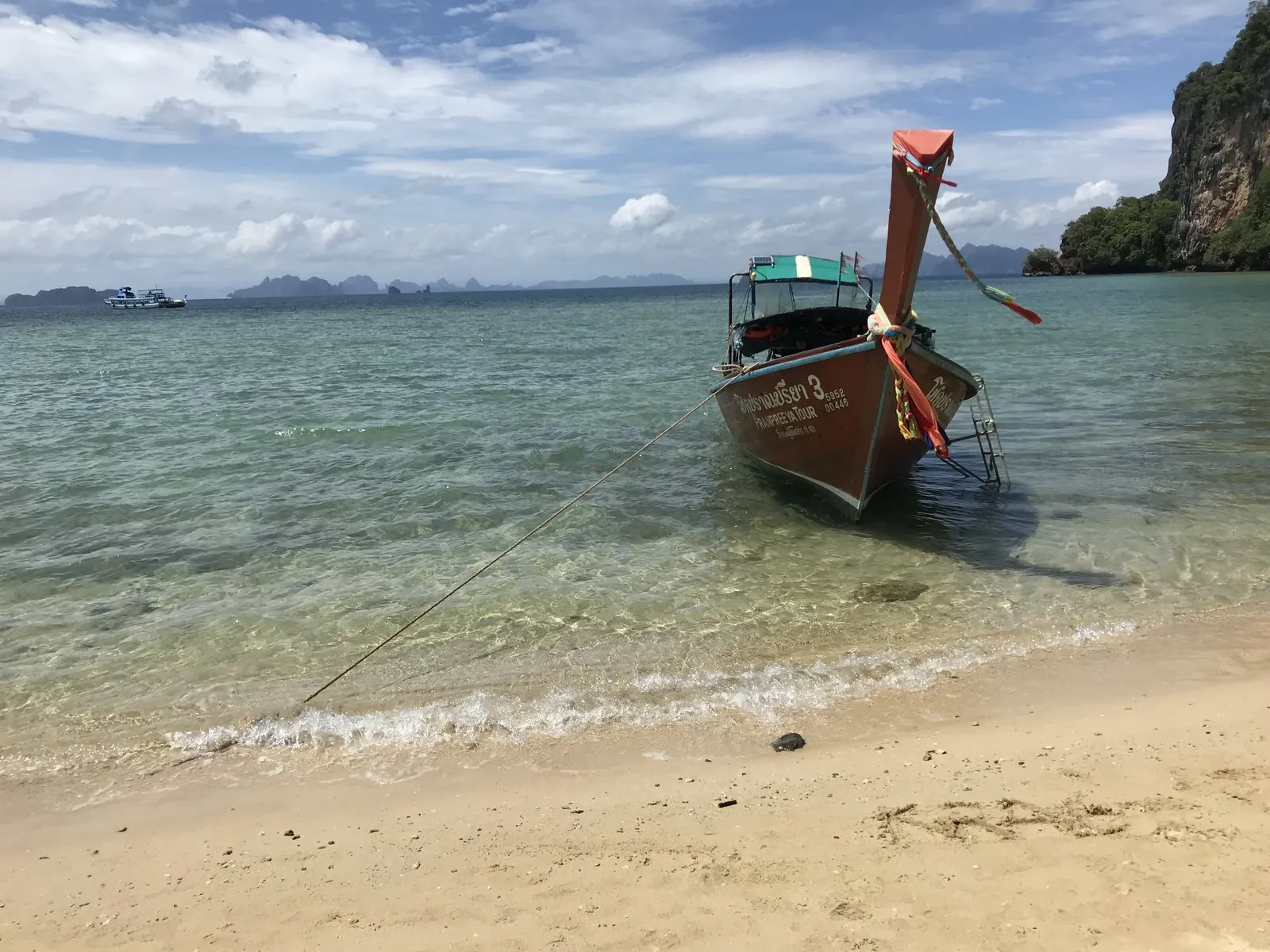 浅瀬に浮かぶロングテールボート。船首に布が巻かれ、背後に石灰岩の島がそびえる