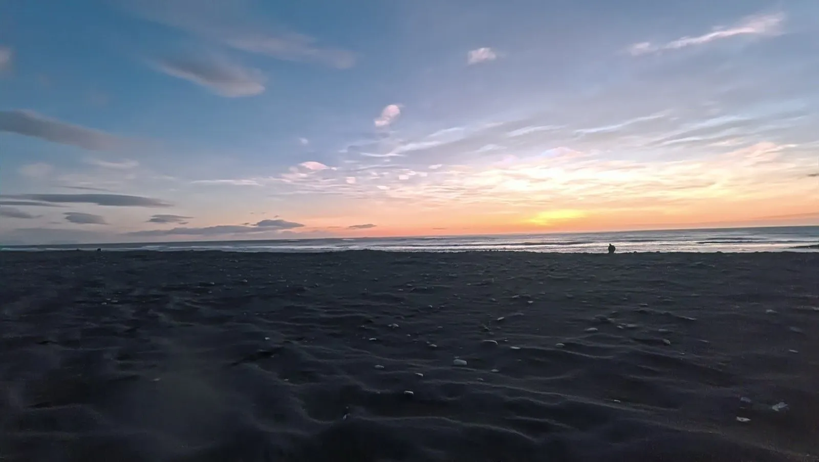 黒い砂浜の先に夕焼けの空と波が広がっている