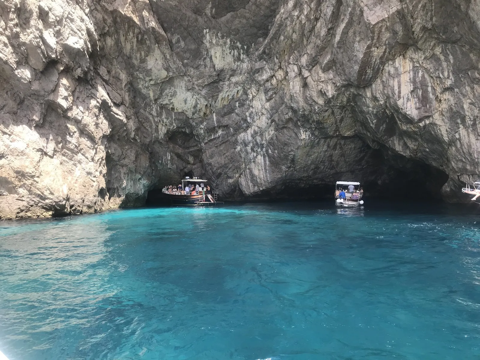 大きな洞口に入っていく観光ボートと、透けたターコイズブルーの海