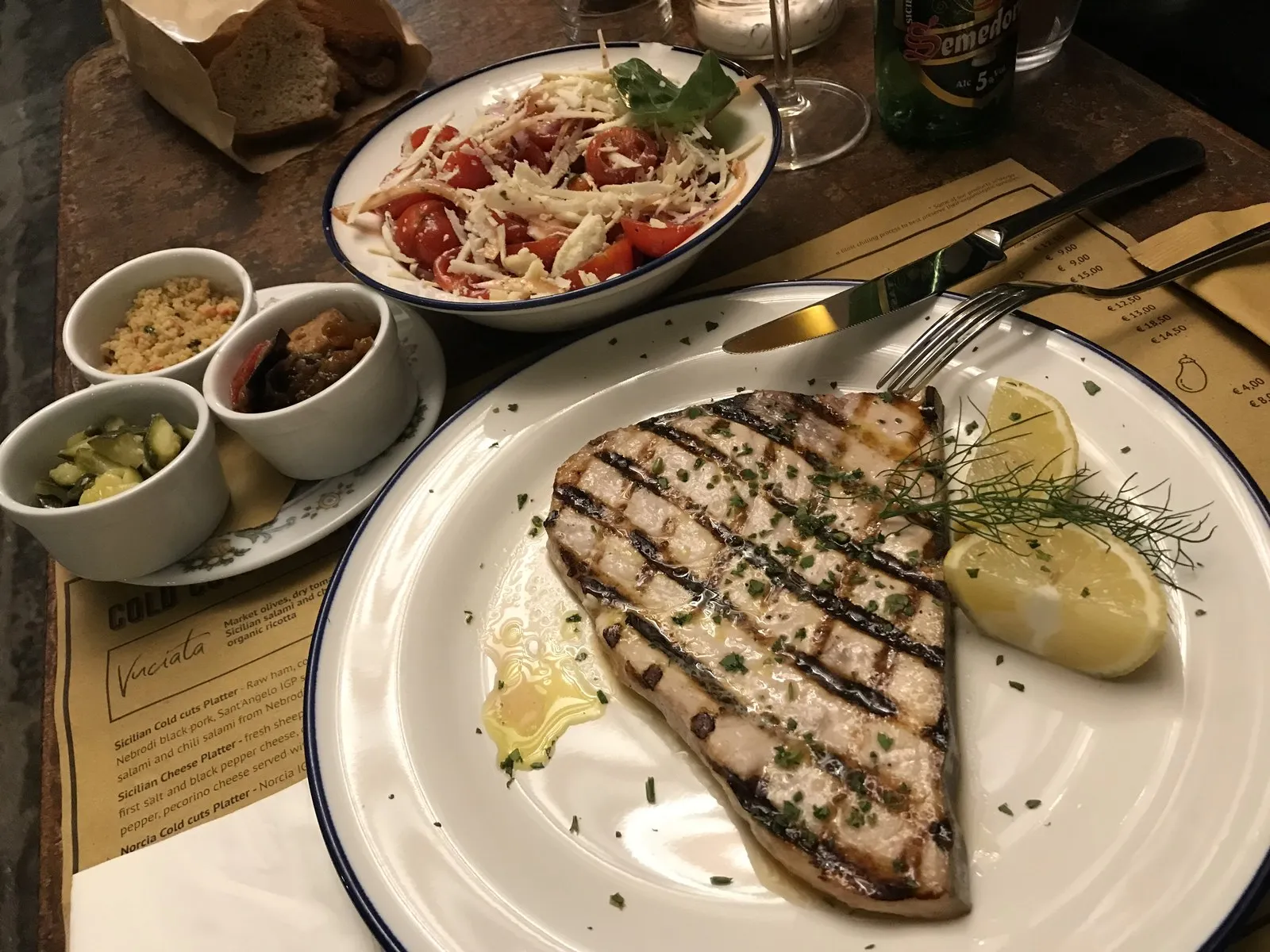 グリルしたカジキのステーキ、副菜、パン、飲み物が並んだテーブル