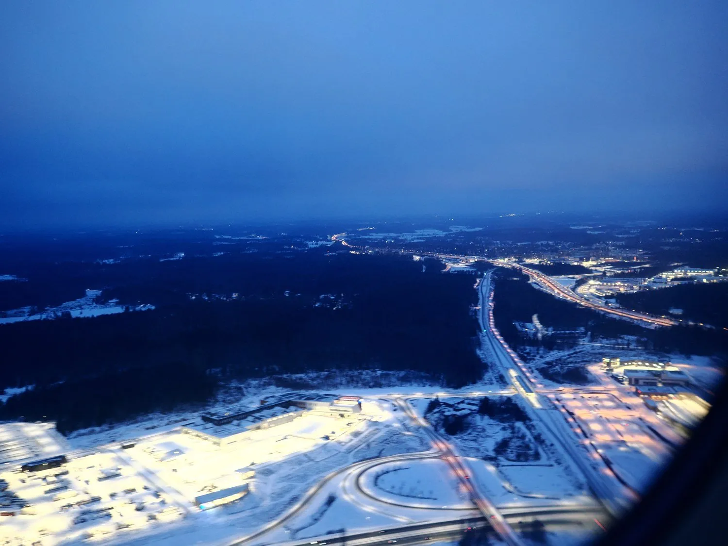 飛行機の窓から見た夜明け前の街。雪の地面に道路の明かりが線になって伸びている