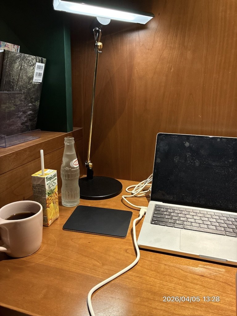 夕方の作業デスク。デスクライトが点灯し、コーヒーとジュースが置いてある